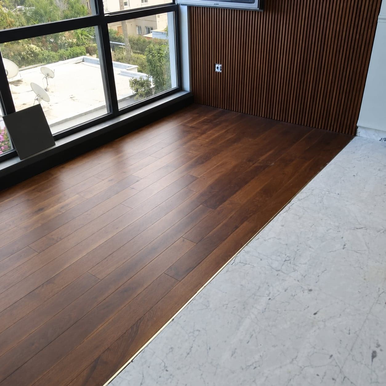 Vue du parquet brun, de la fenêtre et de la transition vers un sol clair. Version retouchée par IA.